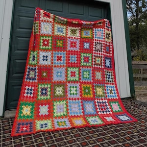May include: A large rectangular quilt featuring a vibrant red grid pattern that separates numerous square blocks. Each block contains a variety of colorful fabric patches in shades of blue, green, yellow, and pink, arranged in a geometric design.