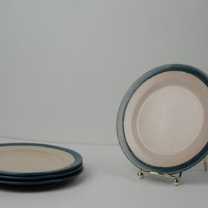 Könnte beinhalten: Set aus vier weißen Keramiktellern mit blauem Rand. Die Teller sind übereinander gestapelt.