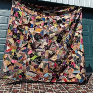 May include: A large, rectangular crazy quilt constructed from numerous irregular fabric scraps in a wide variety of colors, textures, and patterns. The pieces are joined together with decorative embroidery stitches along the seams.