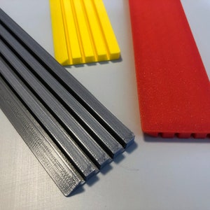 May include: Three strips of plastic, one gray, one yellow, and one red. The gray strip is the longest and has a textured surface. The yellow strip is shorter and has a smooth surface. The red strip is the shortest and has a textured surface.