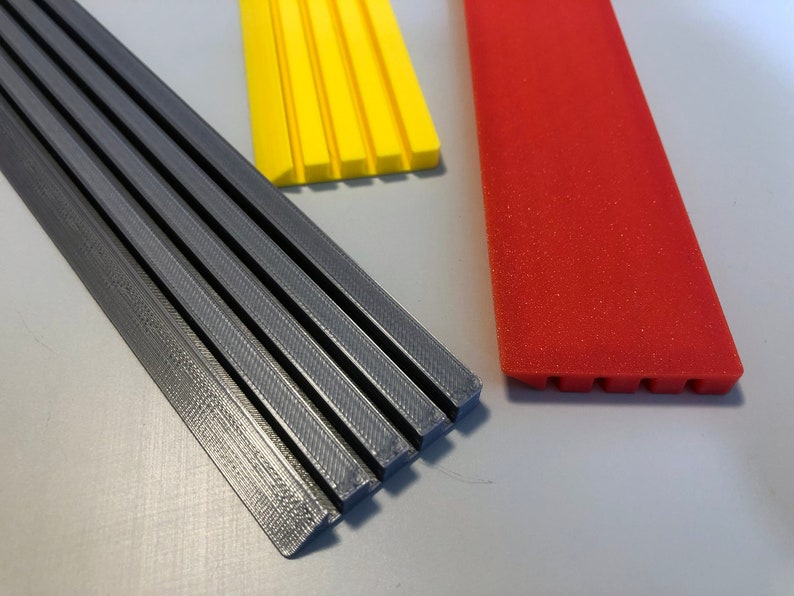 May include: Three strips of plastic, one gray, one yellow, and one red. The gray strip is the longest and has a textured surface. The yellow strip is shorter and has a smooth surface. The red strip is the shortest and has a textured surface.