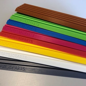 May include: A stack of eight different colored plastic strips with the text "BOARDGAME3DPARTS" printed on each strip.