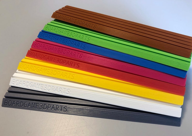 May include: A stack of eight different colored plastic strips with the text "BOARDGAME3DPARTS" printed on each strip.
