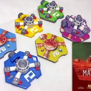 May include: A game board with six hexagonal tiles, each featuring a different colored space station with a central hub and four arms. The tiles are arranged in a circle around a box cover with the title "On Mars".