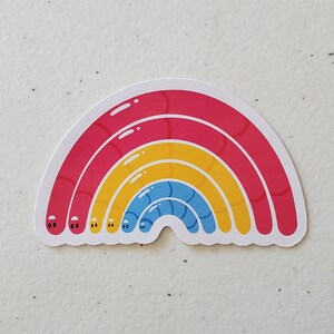 May include: A rainbow sticker with three layers of colour: red, yellow, and blue. Each layer has a slightly different texture, giving the rainbow a 3D effect.