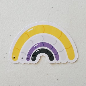 May include: A rainbow-coloured sticker with three curved lines in yellow, white, purple, and black. The sticker is shaped like a rainbow arch.