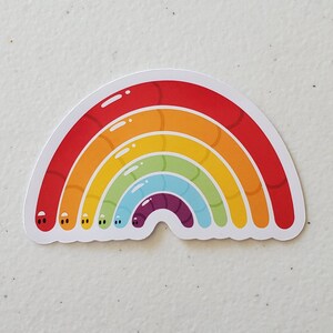 May include: A rainbow sticker featuring a worm design. The rainbow is made up of red, orange, yellow, green, blue, purple, and indigo worms. Each worm has two small black eyes.
