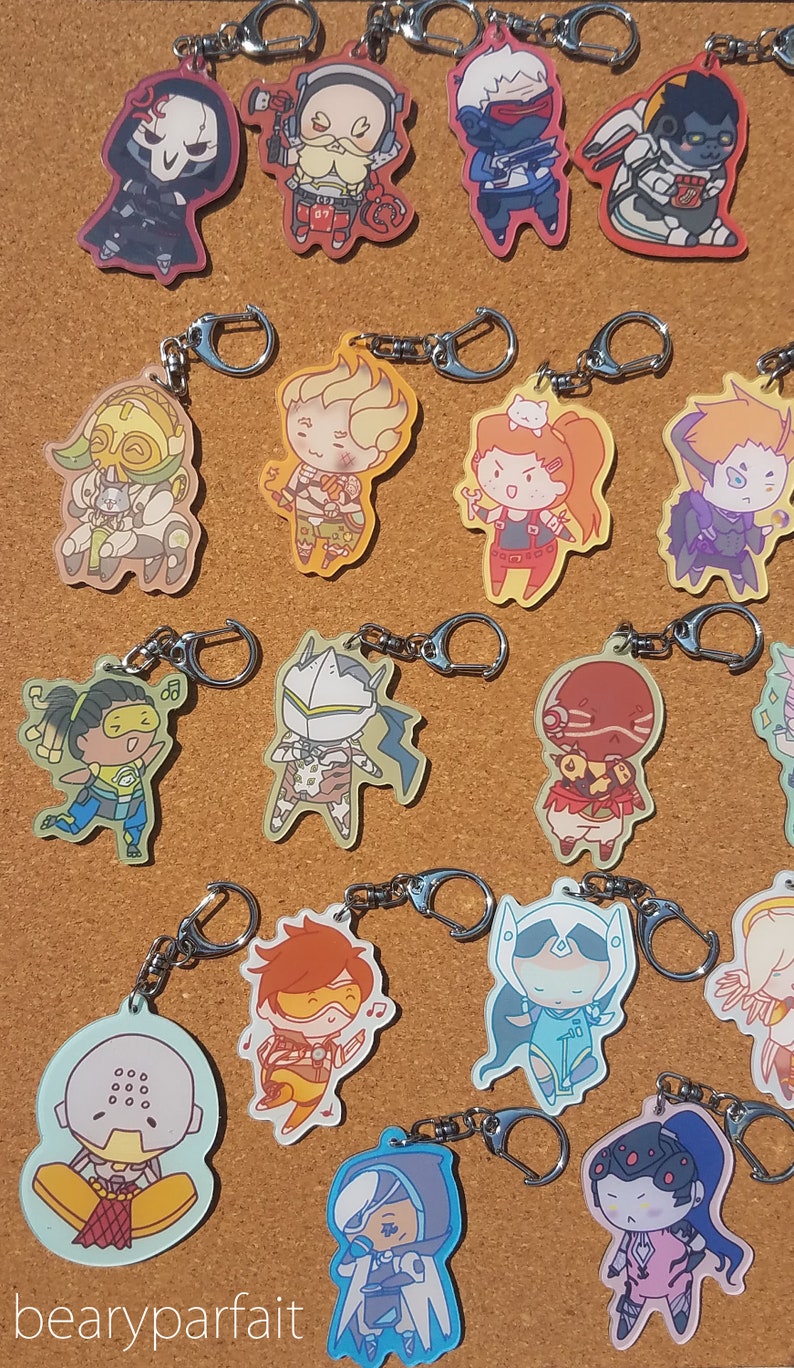 May include: A collection of Overwatch character keychains featuring various characters from the game, including Reaper, Soldier: 76, Tracer, D.Va, Genji, Mercy, Reinhardt, Symmetra, Torbjorn, Widowmaker, and more. The keychains are made of clear acrylic and feature colorful illustrations of the characters.