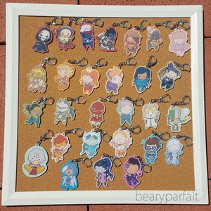 May include: A corkboard with a variety of colorful keychains featuring cartoon characters. The keychains are attached to the corkboard with metal rings. The corkboard is framed in white and has the text "bearyparfait" written on the bottom right corner.