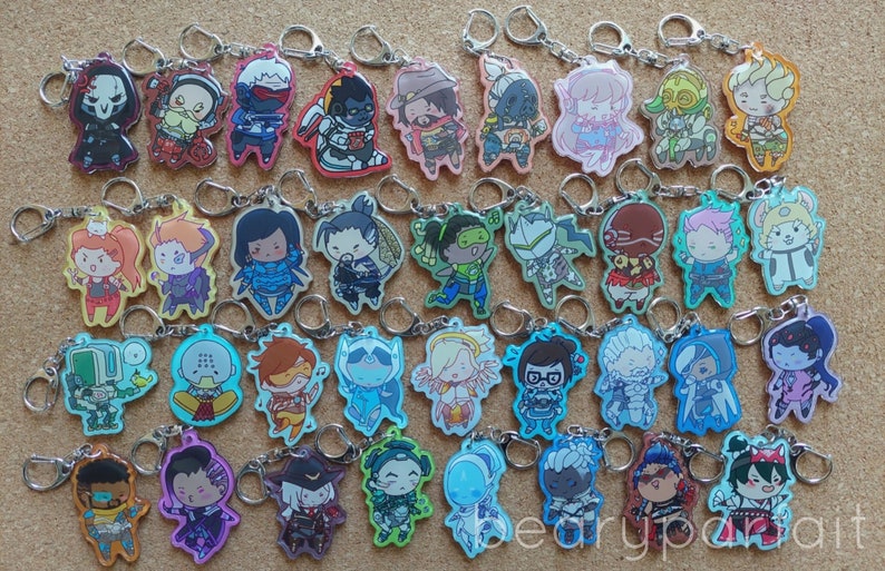 May include: A collection of 40 colorful Overwatch character keychains. Each keychain features a different character from the game, including Reaper, D.Va, Tracer, and Genji. The keychains are made of clear acrylic and have a glossy finish.