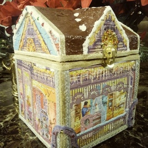 May include: A gingerbread house-shaped wooden box with a gold latch and purple trim. The box is decorated with a winter scene and a snowy roof.