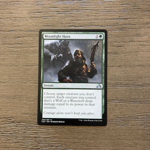 May include: A green and black Magic: The Gathering card with the title "Moonlight Hunt". The card depicts a man with a crossbow in a forest. The text on the card reads: "Choose target creature you don't control. Each creature you control that's a Wolf or a Werewolf deals damage equal to its power to that creature. Courage alone won't keep you alive."