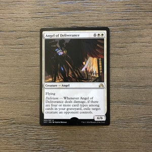 May include: A white bordered card with a black background featuring an illustration of an angel with black wings and a white robe. The card is titled "Angel of Deliverance" and has a 6/6 power and toughness rating. The card text reads "Flying, Delirium - Whenever Angel of Deliverance deals damage, if there are four or more card types among cards in your graveyard, exile target creature an opponent controls."