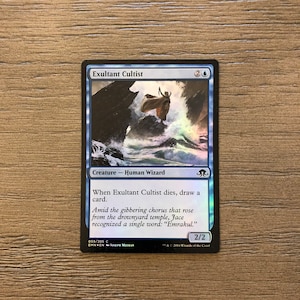 May include: A blue and white Magic: The Gathering card featuring a wizard standing on a rock in a stormy sea. The card is titled "Exultant Cultist" and has a mana cost of 2 blue. The card text reads: "Creature - Human Wizard. When Exultant Cultist dies, draw a card. Amid the gibbering chorus that rose from the drownyard temple, Jace recognized a single word: "Emrakul." 2/2"