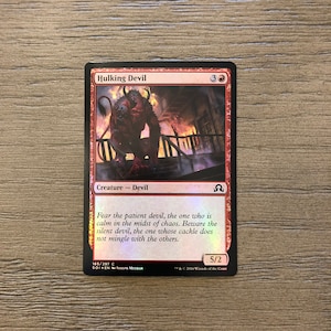 Puede incluir: Una carta roja Hulking Devil de Magic: The Gathering con un fondo rojo y una ilustración roja y negra de un diablo. El texto de la carta dice "Teme al diablo paciente, el que está tranquilo en medio del caos. Ten cuidado con el diablo silencioso, aquel cuya risa no se mezcla con los demás." La carta tiene una fuerza de 5 y una resistencia de 2.