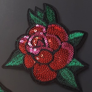 May include: Embroidered rose patch with red sequins and green leaves. The rose petals are covered in shiny red sequins, with pink sequins at the center. The leaves are green with black stitching.