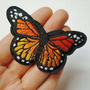 May include: Embroidered butterfly patch with black, orange, and yellow wings. The butterfly has white accents around the edges of the wings.