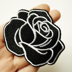 May include: Black embroidered rose patch with white outline. The rose is a classic floral design and can be used to decorate clothing, bags, or other items.