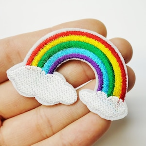 May include: Embroidered rainbow patch featuring a vibrant arc of red, orange, yellow, green, blue, and purple. The rainbow is set against two fluffy white cloud shapes. This patch is ideal for adding a colorful touch to clothing or accessories.