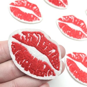 May include: Embroidered red lips patches with white borders. The patches feature a detailed design of open lips, perfect for adding a touch of flair to clothing, bags, or accessories. The patches are set against a white background.