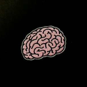 May include: Embroidered patch featuring a pink brain with black outlines and a light gray border. The brain design is detailed and sits against a solid black background. This patch is suitable for jackets, bags, or other fabric items.