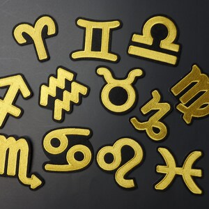 May include: Twelve gold embroidered zodiac signs on a black background. The signs are Aries, Taurus, Gemini, Cancer, Leo, Virgo, Libra, Scorpio, Sagittarius, Capricorn, Aquarius, and Pisces.
