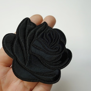 May include: Black embroidered rose patch. The rose is detailed with multiple layers of petals.