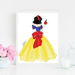May include: A framed illustration of a woman in a yellow gown, holding a red apple. The woman has black hair and a red bow. The illustration is in a white frame, with pink flowers and a birdcage in the background.