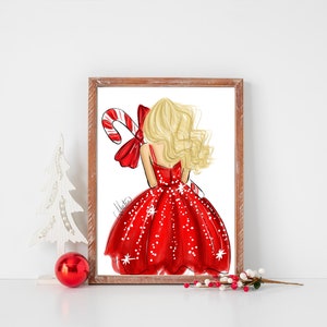 Op de afbeelding: Een ingelijste print met een mode-illustratie van een vrouw in een rode jurk met witte sneeuwvlokaccenten, die een zuurstok vasthoudt. De vrouw heeft blond haar en een rode strik. Het kunstwerk staat tegen een witte achtergrond.