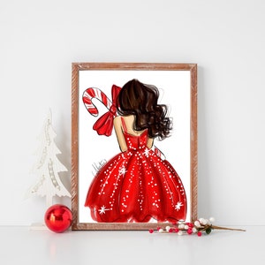 Op de afbeelding: Een ingelijste illustratie van een vrouw in een rode jurk met witte stippen, met een zuurstok en strik. Het kunstwerk heeft een kerstthema, met een witte kerstboom en rode bal op de voorgrond.