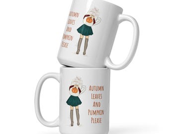 May include: Two white ceramic mugs stacked on top of each other. Each mug features a whimsical illustration of a person holding a pumpkin and the text "AUTUMN LEAVES AND PUMPKIN PLEASE" in orange and brown.