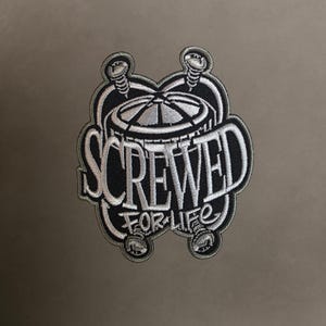 May include: Embroidered patch with the words "SCREWED FOR LIFE" in white, outlined in black. The design includes a stylized gear and screws, set against a neutral background. The patch is likely for clothing or accessories.