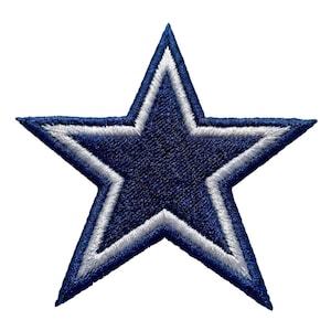 May include: Embroidered navy blue star with a white outline. The star has a five-point design and is likely a patch or emblem. The stitching is detailed, and the star is set against a white background.