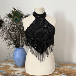 May include: A black halter top with sequins and fringe. The top is on a white mannequin.