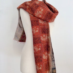 May include: A red and white patterned scarf with a geometric design. The scarf is made of silk and has a fringed edge.