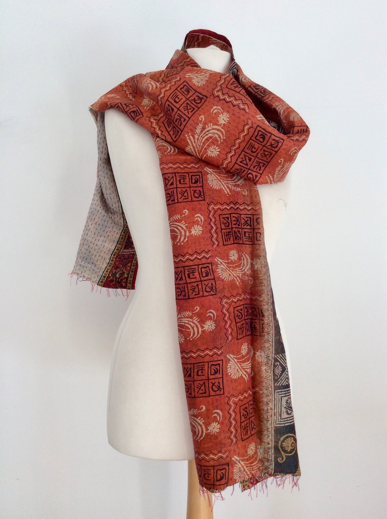 May include: A red and white patterned scarf with a geometric design. The scarf is made of silk and has a fringed edge.