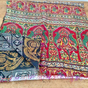 May include: A colorful kantha quilt with a red, green, and gold paisley pattern. The quilt is folded in half and has a fringed edge.