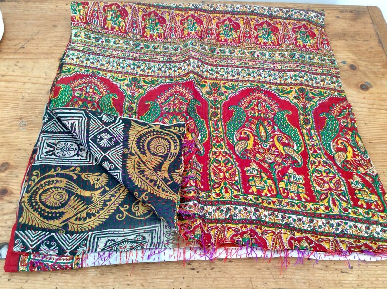 May include: A colorful kantha quilt with a red, green, and gold paisley pattern. The quilt is folded in half and has a fringed edge.