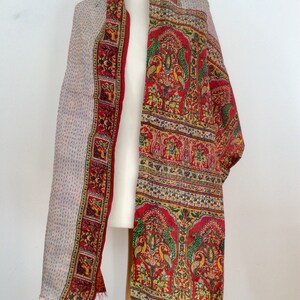 May include: A red and white silk scarf with a paisley pattern and floral designs. The scarf is fringed on the edges.
