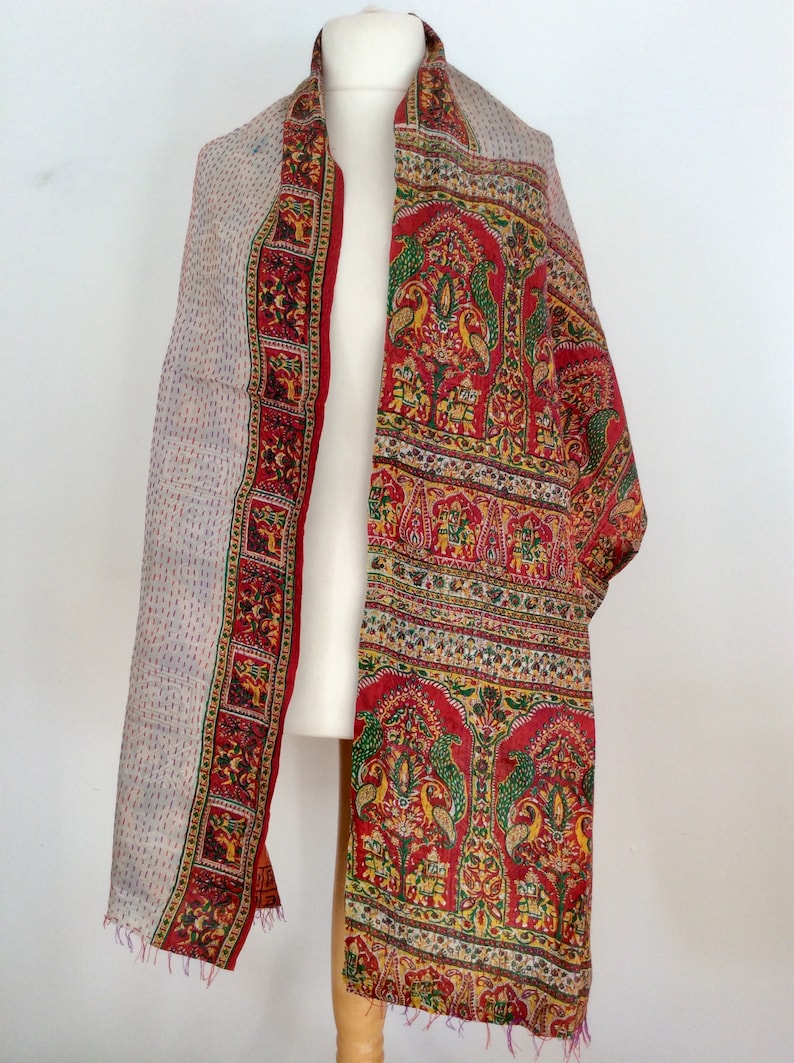 May include: A red and white silk scarf with a paisley pattern and floral designs. The scarf is fringed on the edges.