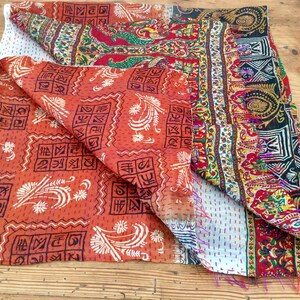 May include: A colorful kantha quilt with a patchwork design. The quilt is made of different fabrics with various patterns, including floral, geometric, and paisley motifs. The quilt is folded in half, revealing the intricate stitching and the different layers of fabric.