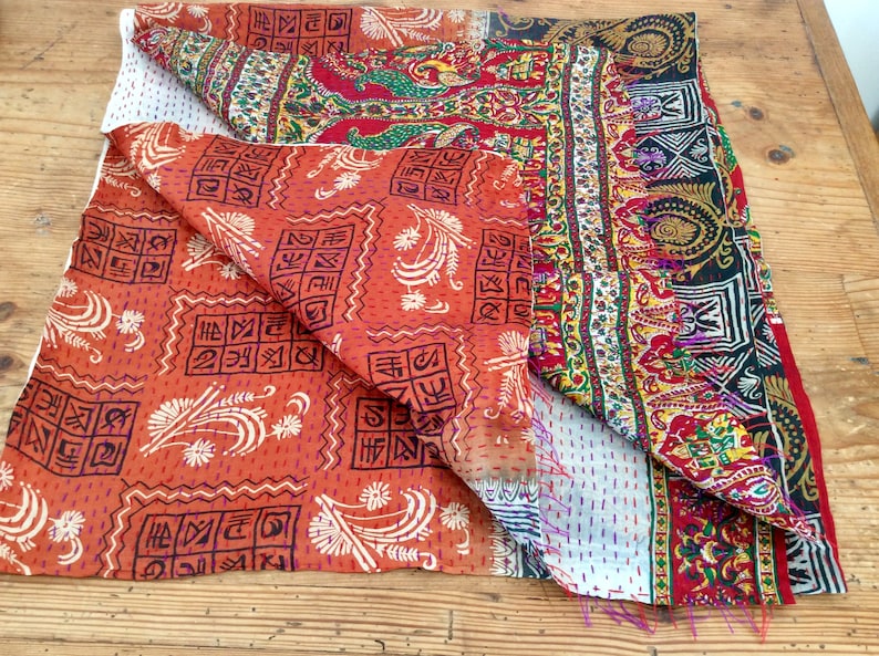 May include: A colorful kantha quilt with a patchwork design. The quilt is made of different fabrics with various patterns, including floral, geometric, and paisley motifs. The quilt is folded in half, revealing the intricate stitching and the different layers of fabric.