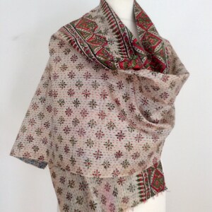 May include: A white cotton kantha shawl with a red, green, and blue floral pattern. The shawl is folded and draped over a mannequin.