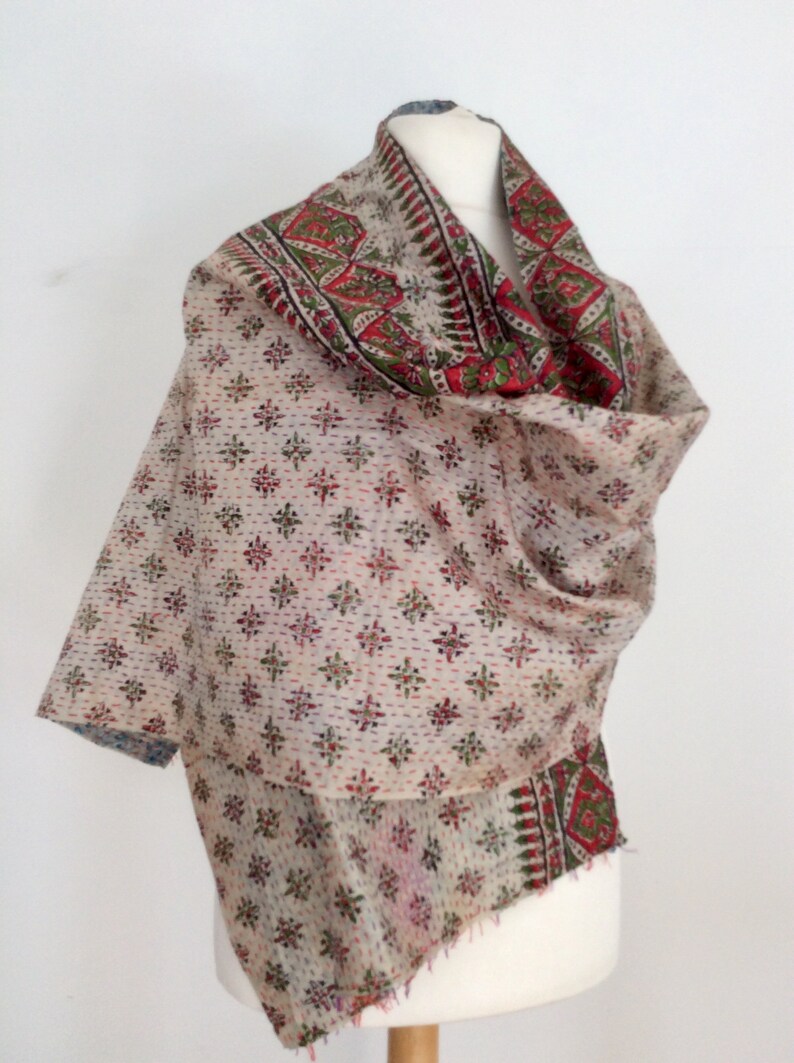 May include: A white cotton kantha shawl with a red, green, and blue floral pattern. The shawl is folded and draped over a mannequin.
