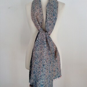 May include: A light blue and cream patterned scarf with a textured woven design. The scarf is tied around a white mannequin.