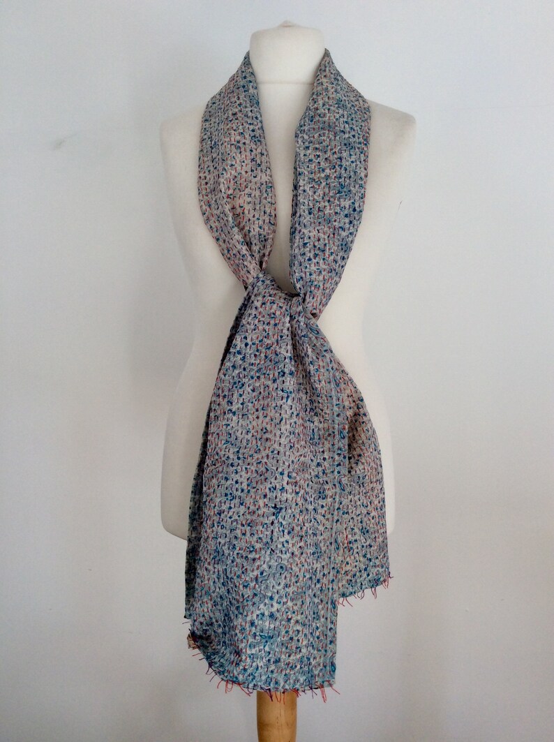 May include: A light blue and cream patterned scarf with a textured woven design. The scarf is tied around a white mannequin.