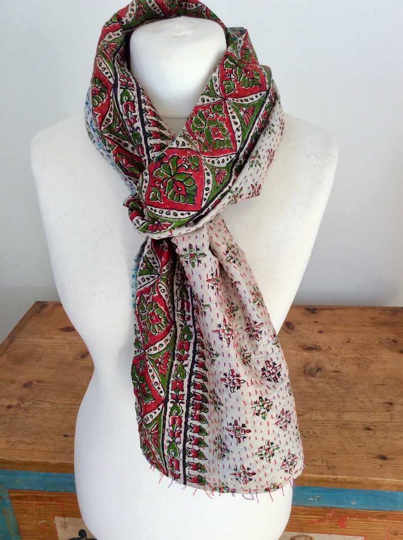 May include: A white silk scarf with a red, green, and blue floral pattern. The scarf is tied around a white mannequin's neck.