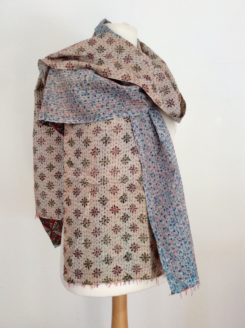 May include: A beige, blue, and red kantha quilt scarf with a geometric pattern. The scarf is draped over a white mannequin.