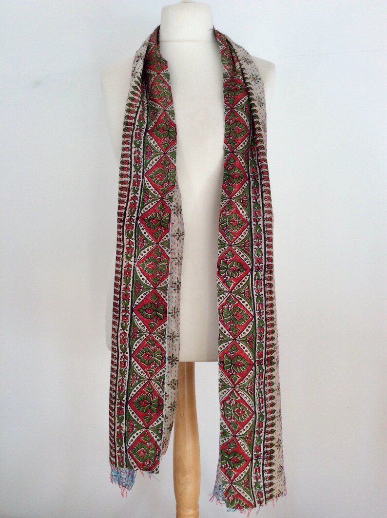 May include: A long, white scarf with a red, green, and black patterned border. The scarf is made of a soft, lightweight fabric and is perfect for adding a touch of color to any outfit.