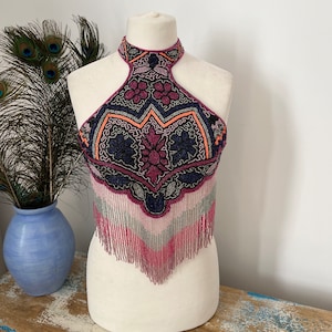 Può includere: Un top halter con perline con un motivo geometrico in tonalità rosa, viola, blu e nero. Il top ha un bordo a frangia e un'apertura a chiave nella parte posteriore.